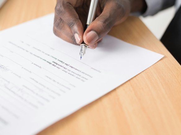 Close up of hands signing real estate property closing documents with a pen on an office desk.