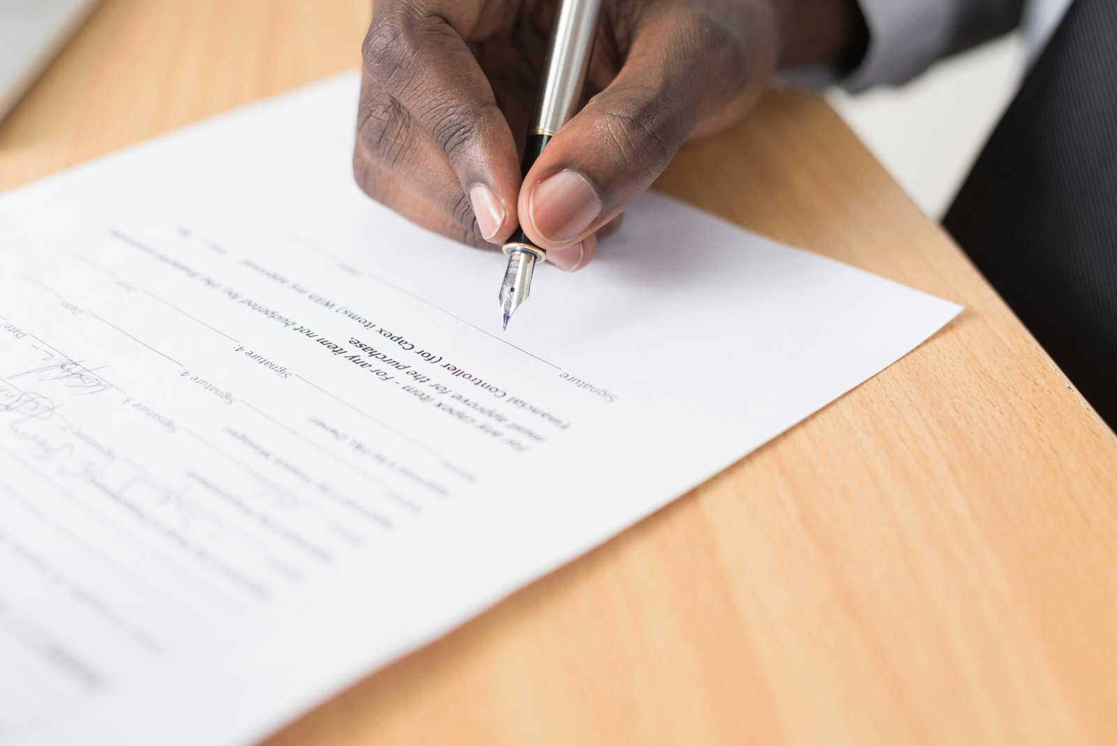 Close up of hands signing real estate property closing documents with a pen on an office desk.